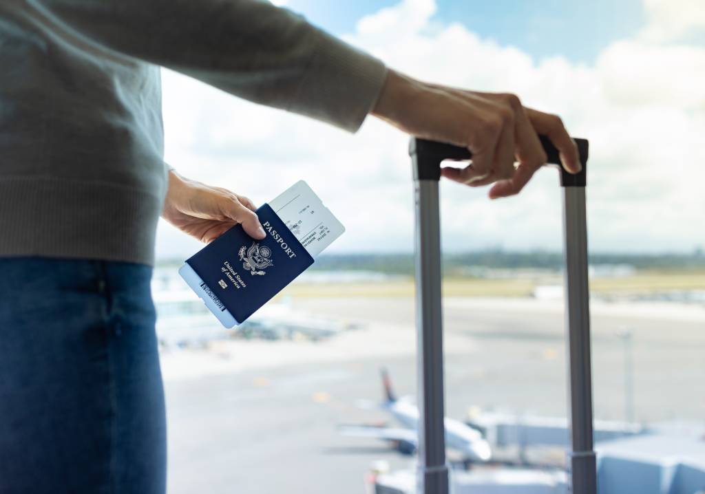 A person’s hand holding a passport and a suitcase